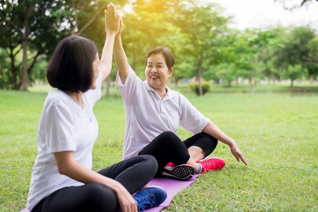 Concepto de estilo de vida saludable, las mujeres asiáticas levantan las manos y se relajan en el parque por la mañana juntas, felices y sonrientes, pensamiento positivo