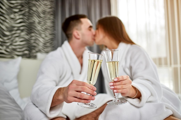 Concepto de estilo de vida saludable de spa de belleza Hermosa pareja joven en batas de baño relajándose en una habitación de hotel de lujo El niño y la niña descansan en un lugar acogedor y beben vino Tema de bienestar