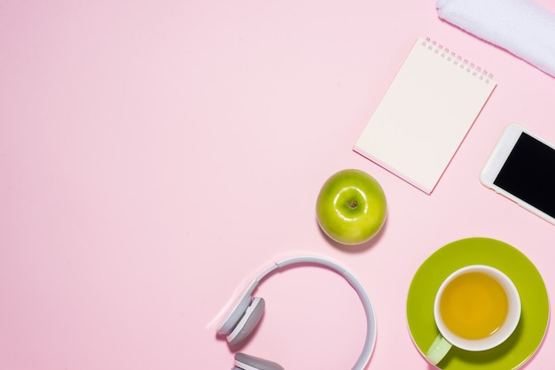 Concepto de estilo de vida saludable. Zapatillas, té, manzana y auriculares sobre fondo de color pastel.