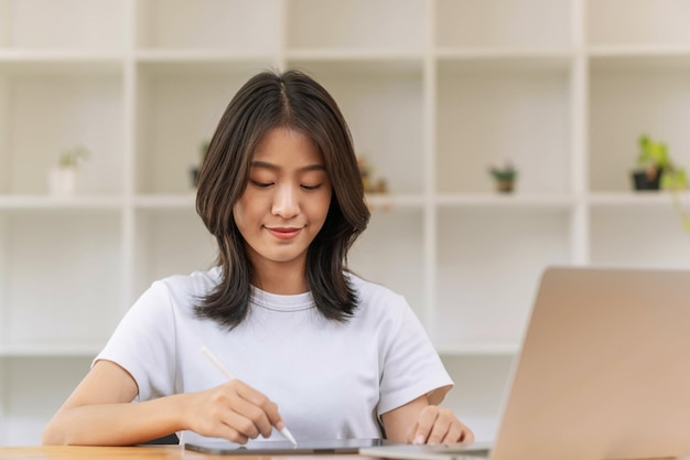 Concepto de estilo de vida y tecnología Mujer asiática joven escribiendo en tableta y usando una computadora portátil para trabajar