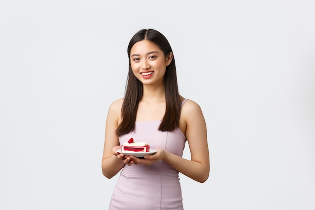 Concepto de estilo de vida, vacaciones, celebración y comida. Hermosa mujer asiática en vestido de fiesta, disfrutando celebrando el cumpleaños de un amigo