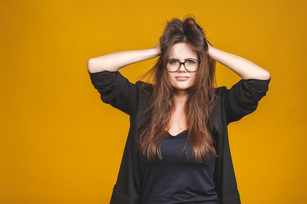 Concepto de estrés Una mujer de negocios muy frustrada y enojada tirando de su cabello. Aislado contra amarillo.