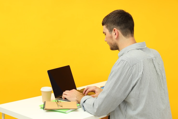 Foto concepto de estudio con joven sentado en la mesa sobre fondo amarillo.