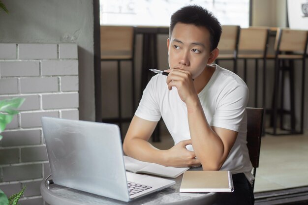 Concepto de estudio en línea el joven de simple camiseta blanca es reflexivo y serio frente a la pantalla durante la clase en línea.