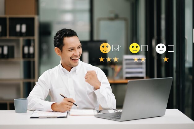 Concepto de evaluación de servicio al cliente Empresario asiático presionando cara emoticon de sonrisa en pantalla virtual en tableta y teléfono inteligentexA
