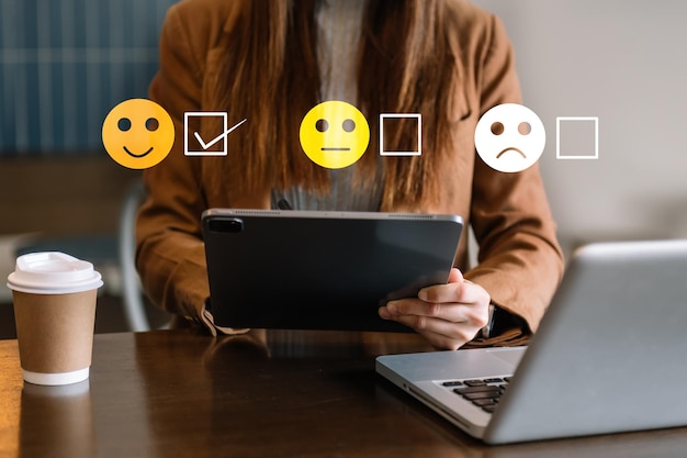 Concepto de evaluación del servicio al cliente Mujer Mostrar emoticono de sonrisa en la pantalla virtual desde la mano mirando la tableta del teléfono inteligente y la computadora portátil en la oficina
