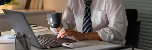 Concepto de exceso de trabajo Un oficinista que trabaja hasta tarde bebiendo una taza de café mientras se concentra en el trabajo