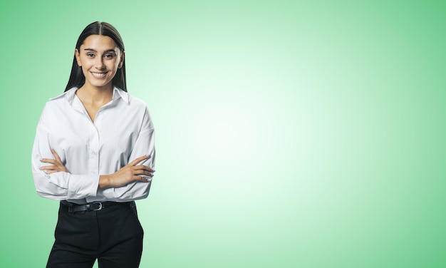 Concepto de éxito empresarial con una joven empresaria sonriente doblando las manos con camisa blanca y pantalón negro sobre un fondo verde claro abstracto con lugar para su logotipo o texto Mock up