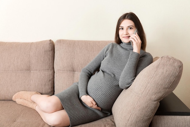 Concepto de expectativa de embarazo mujer embarazada feliz hablando por teléfono inteligente en casa