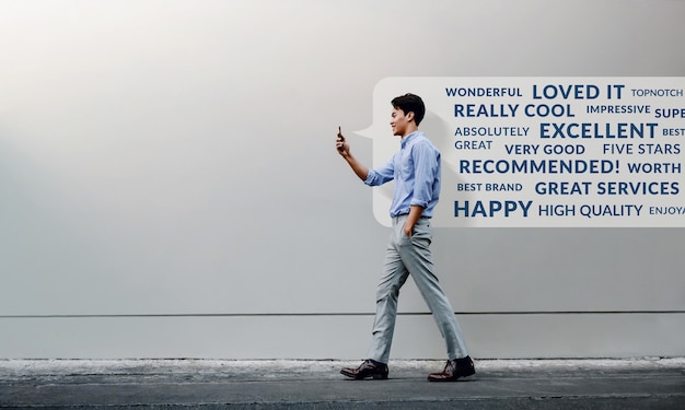Concepto de experiencia del cliente. leer reseña positiva en línea a través de un teléfono inteligente. sonriente joven empresario con teléfono móvil mientras camina por la pared del edificio urbano.