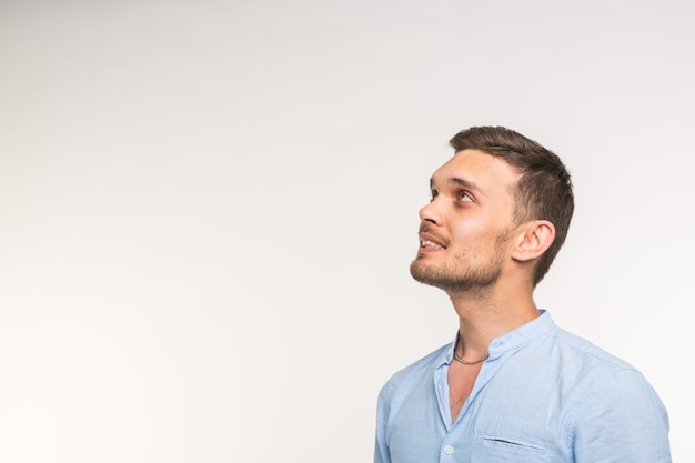 Foto concepto de expresiones y personas - apuesto joven alegre mirando hacia arriba sobre la pared blanca con espacio de copia.