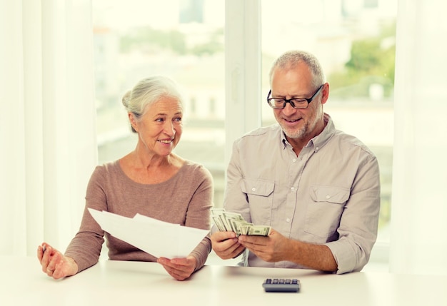 concepto de familia, ahorro, edad y personas - pareja senior sonriente con papeles, dinero y calculadora en casa