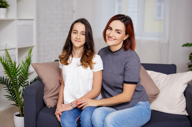 Concepto de familia y amor - madre e hija sonrientes sentadas en la sala de estar