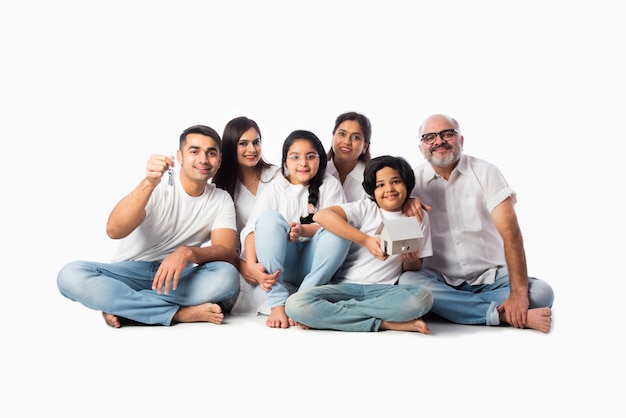 Concepto de familia y bienes raíces indio - familia asiática multigeneracional con modelo de casa de papel con llaves sobre fondo blanco