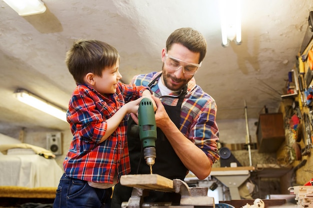 Foto concepto de familia, carpintería, carpintería y personas - padre e hijo pequeño con tablones de madera perforados en el taller