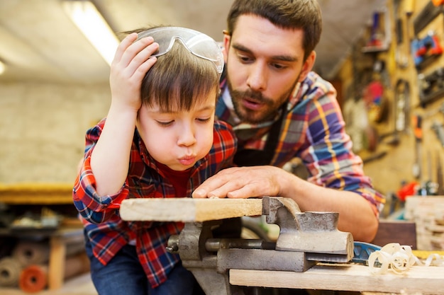 concepto de familia, carpintería, carpintería y personas - padre e hijo pequeño trabajando con tablones de madera en el taller