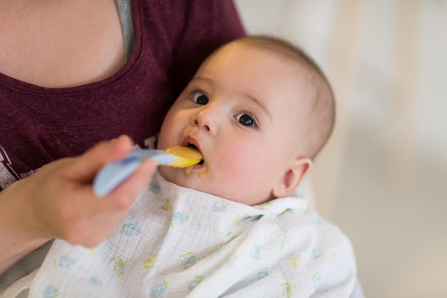 concepto de familia, comida, niño, alimentación y paternidad madre con cuchara alimentando a un bebé en casa