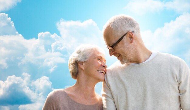 concepto de familia, edad, amor, relaciones y personas - feliz pareja mayor sobre el cielo azul y el fondo de las nubes