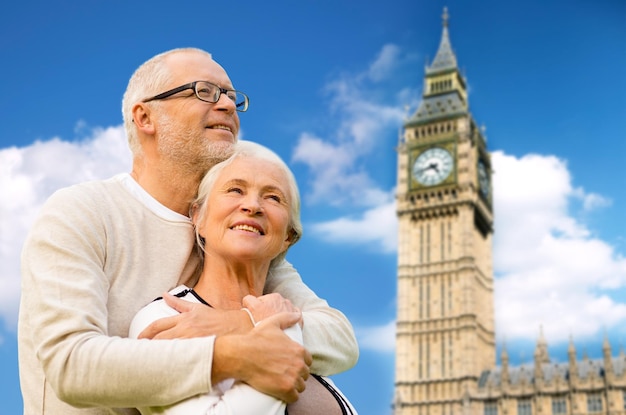 concepto de familia, edad, turismo, viajes y personas - feliz pareja mayor abrazándose sobre la torre del reloj big ben en londres