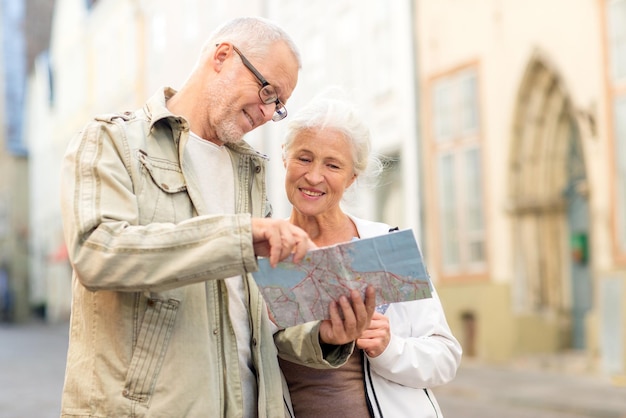 concepto de familia, edad, turismo, viajes y personas - pareja mayor con mapa y guía de la ciudad en la calle