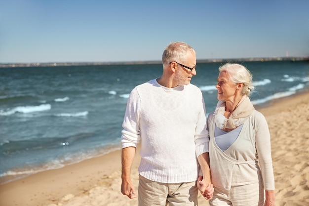 concepto de familia, edad, viajes, turismo y personas - feliz pareja de ancianos caminando por la playa de verano