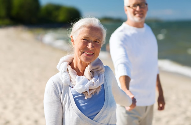 concepto de familia, edad, viajes, turismo y personas - feliz pareja de ancianos tomándose de la mano en la playa de verano