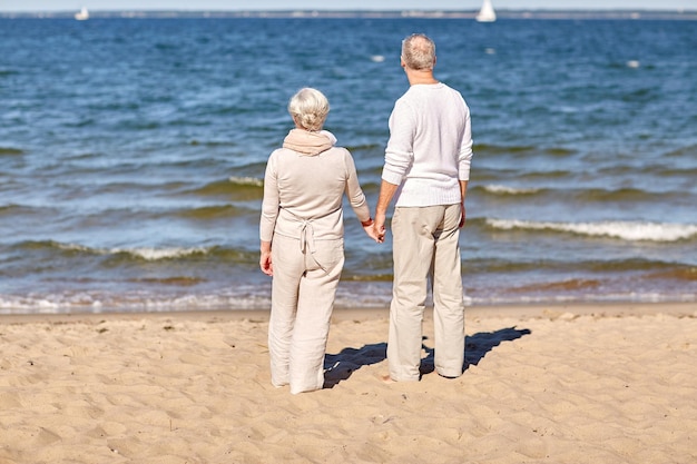 concepto de familia, edad, viajes, turismo y personas - feliz pareja de ancianos tomándose de la mano en la playa de verano