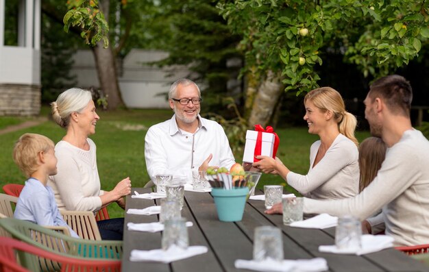 concepto de familia, felicidad, generación, hogar y personas - familia feliz con caja de regalo cenando al aire libre