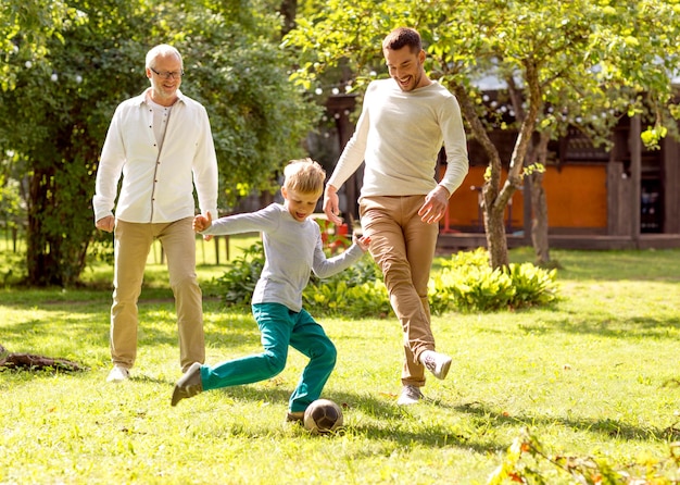 concepto de familia, felicidad, generación, hogar y personas - familia feliz jugando al fútbol frente a la casa al aire libre