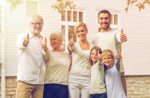 concepto de familia, felicidad, generación, hogar y personas - familia feliz parada frente a la casa al aire libre