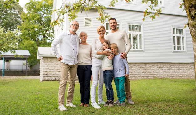 concepto de familia, felicidad, generación, hogar y personas - familia feliz parada frente a la casa al aire libre