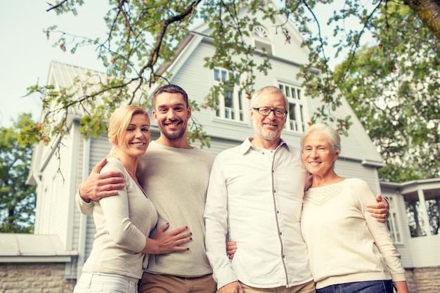 concepto de familia, felicidad, generación, hogar y personas - familia feliz parada frente a la casa al aire libre