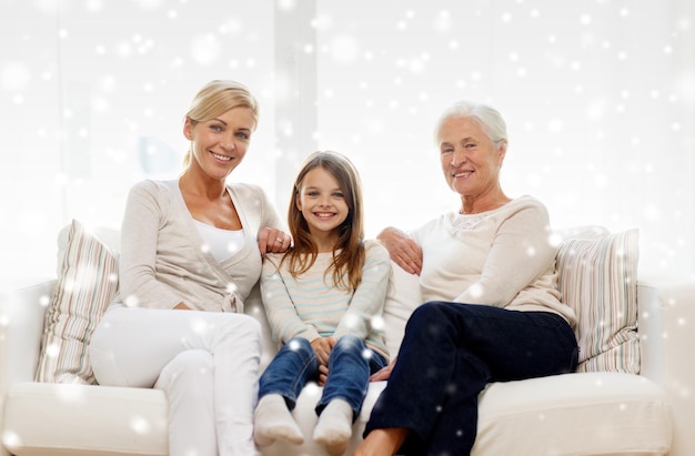 concepto de familia, felicidad, generación y personas - madre sonriente, hija y abuela sentadas en el sofá en casa