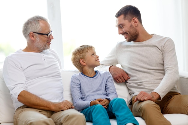 concepto de familia, felicidad, generación y personas - padre, hijo y abuelo sonrientes sentados en el sofá en casa