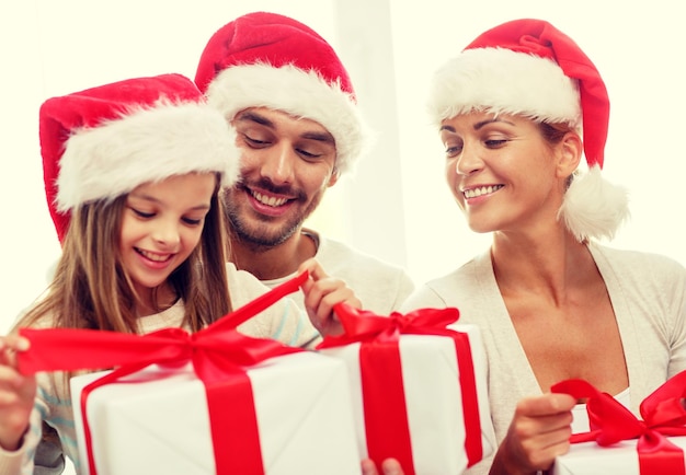 concepto de familia, felicidad, generación, vacaciones y personas - familia feliz con sombreros de ayudante de santa con cajas de regalo sentadas en el sofá en casa