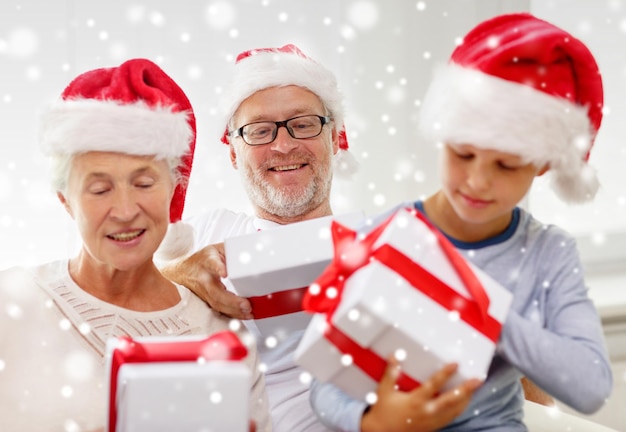 concepto de familia, felicidad, generación, vacaciones y personas - familia feliz con sombreros de ayudante de santa con cajas de regalo sentadas en el sofá en casa