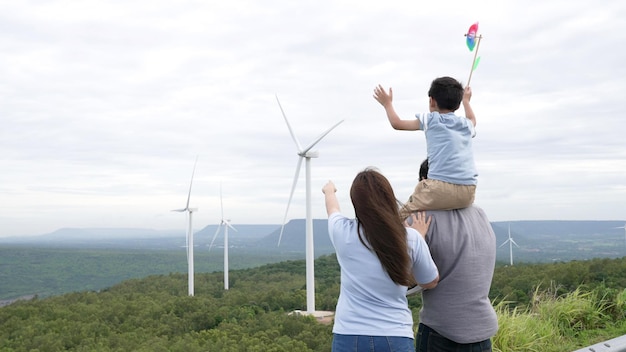 Concepto de familia feliz y progresista disfrutando de su tiempo en el parque de turbinas eólicas Generador eléctrico de viento por generador de turbinas eólicas en el campo con colinas y montañas en el horizonte