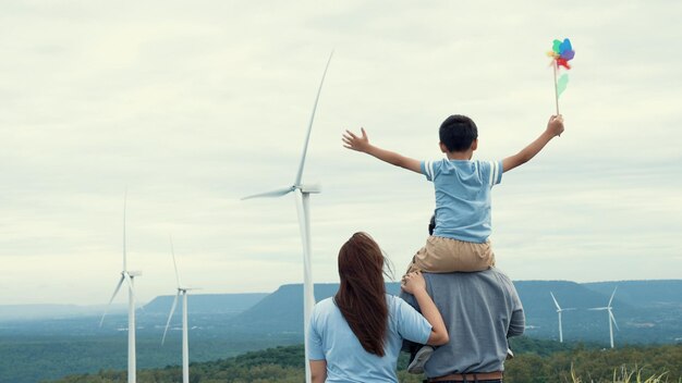 Concepto de familia feliz progresiva disfrutando de su tiempo en la granja de turbinas eólicas Generador eléctrico de viento por generador de turbinas eólicas en el campo con colina y montaña en el horizonte