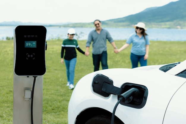 Concepto de familia feliz progresiva en el lago de campo verde con vehículo eléctrico