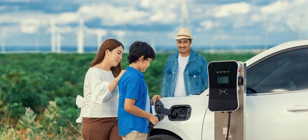 Concepto de familia feliz progresiva en un parque eólico con vehículo eléctrico