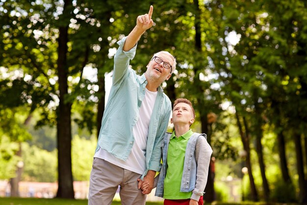 concepto de familia, generación, comunicación y personas - feliz abuelo y nieto caminando y señalando con el dedo en el parque de verano