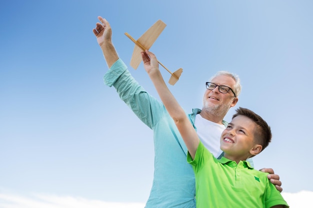 Foto concepto de familia, generación, futuro, sueño y personas - feliz abuelo y nieto con avión de juguete sobre el cielo azul