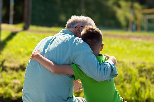 Concepto de familia, generación, relaciones y personas: feliz abuelo y nieto abrazándose al aire libre