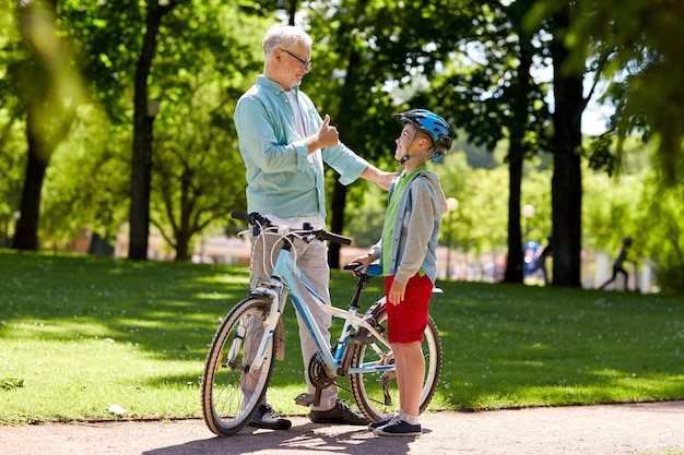 concepto de familia, generación, seguridad y personas - abuelo feliz y niño con casco de bicicleta y bicicleta en el parque de verano