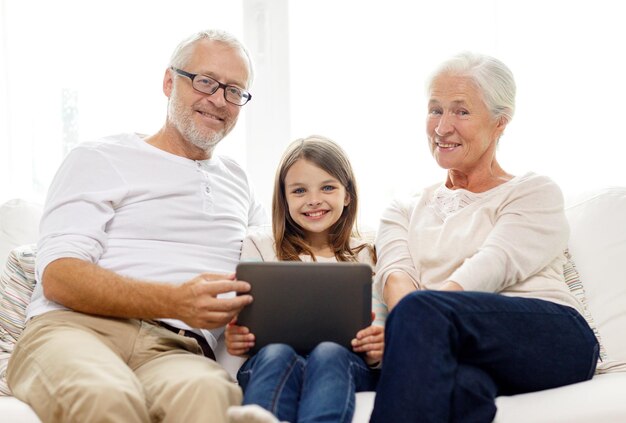 concepto de familia, generación, tecnología y personas: abuelo, nieta y abuela sonrientes con una computadora de tableta sentada en el sofá en casa