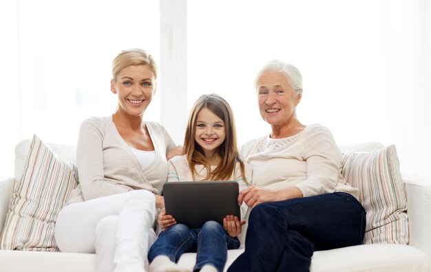 concepto de familia, generación, tecnología y personas: madre, hija y abuela sonrientes con una computadora de tableta sentada en el sofá en casa