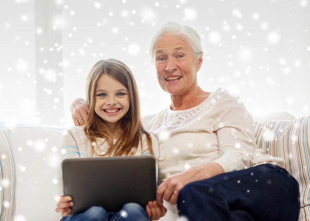 concepto de familia, generación, tecnología y personas - nieta y abuela sonrientes con una computadora de tablet pc sentada en el sofá en casa