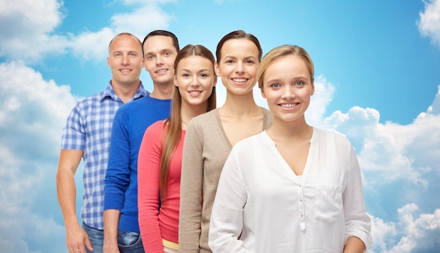 concepto de familia, género y personas - grupo de hombres y mujeres sonrientes sobre el cielo azul y el fondo de las nubes