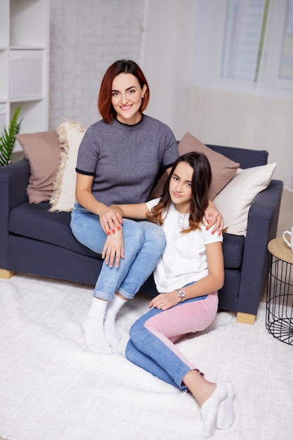 Concepto de familia y hogar - retrato de feliz madre e hija sentada en la sala de estar