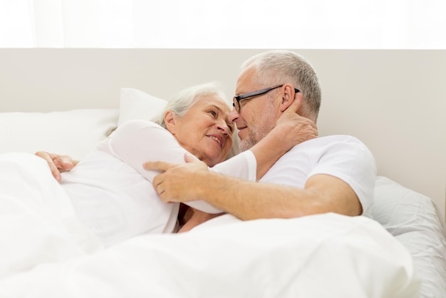 concepto de familia, hora de acostarse, descanso, edad y personas - feliz pareja mayor que yacía mal en casa